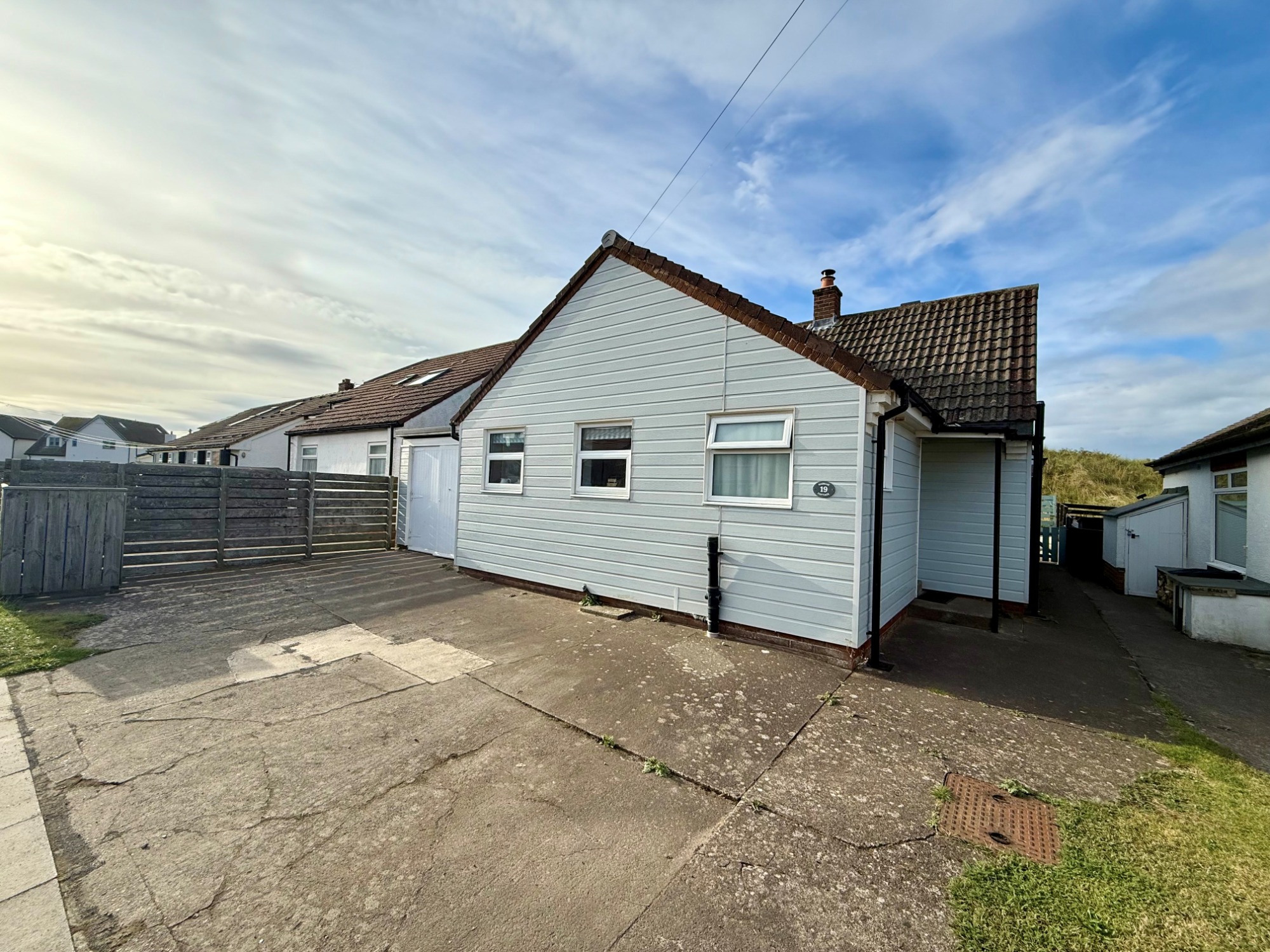 Marram Cottage Beadnell, 3 bedroom self catering family holiday cottage in Northumberland Single-storey white house with a gravel driveway and clear blue sky.