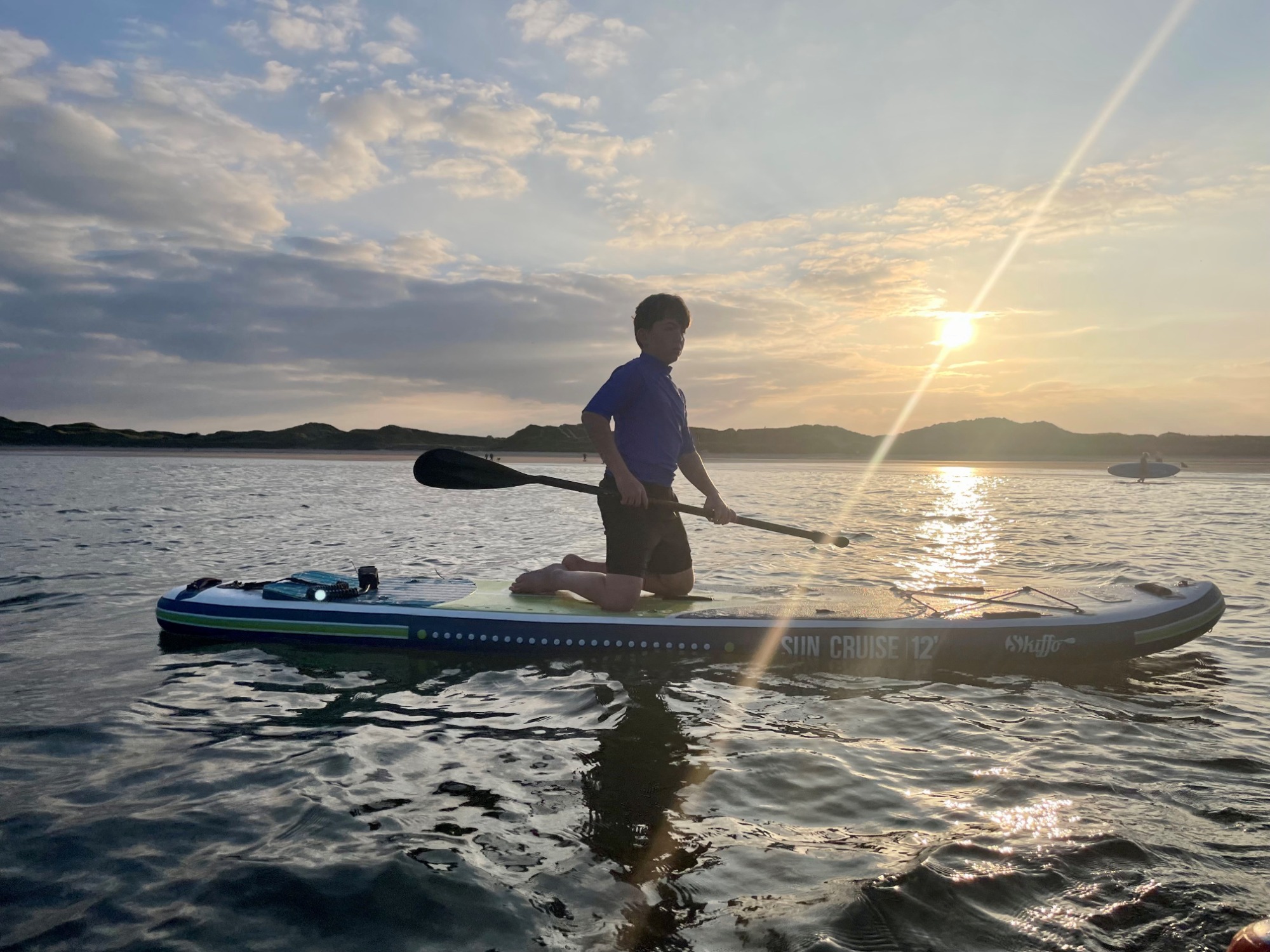 Beadnell Bay watersports Person paddling on a stand-up paddleboard at sunset on a calm water surface.