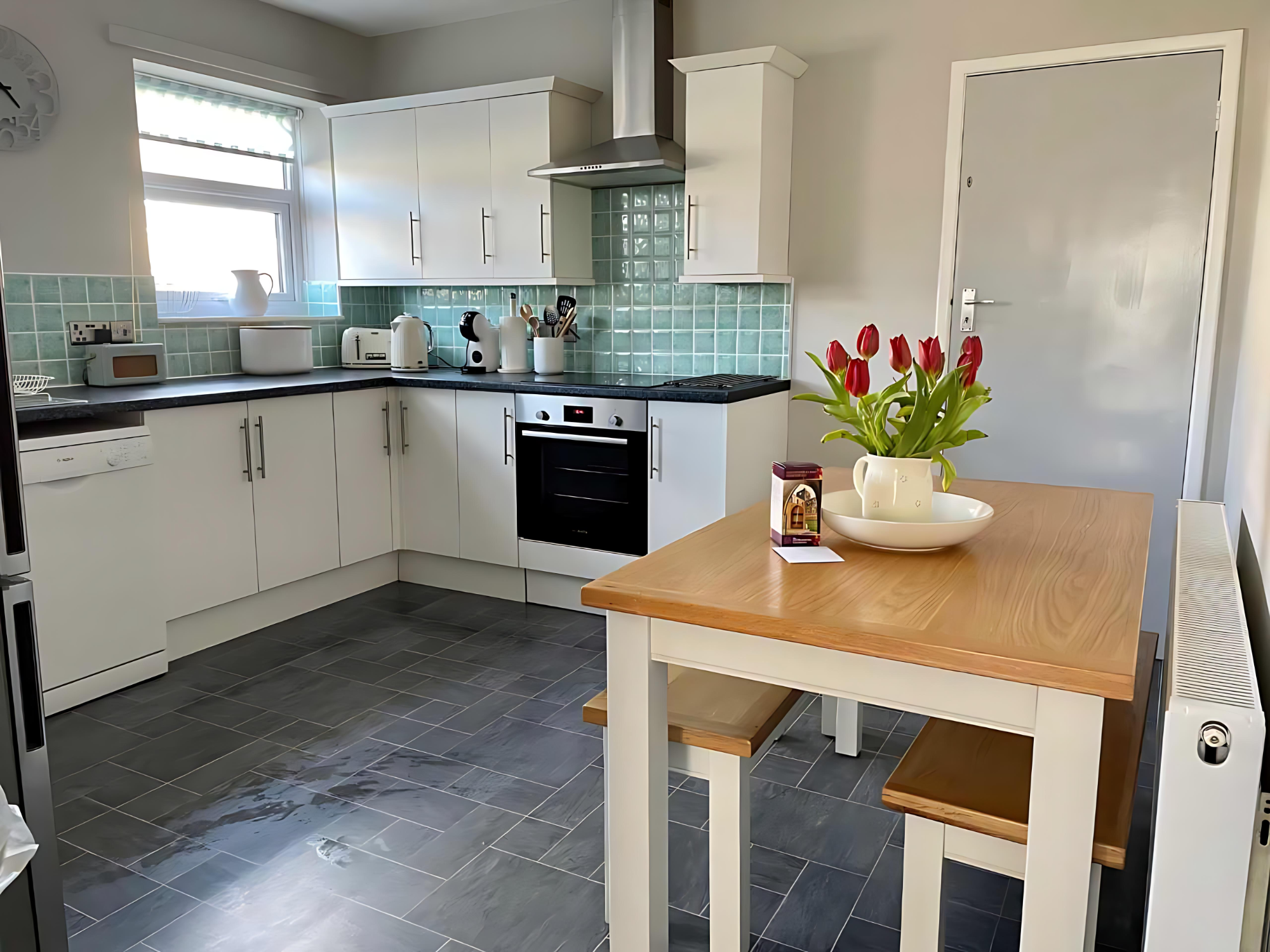 Marram Cottage Beadnell Kitchen Modern kitchen featuring a wooden table with flowers, white cabinets, and grey tiled floor.
